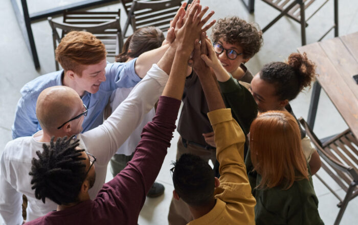 Image shows a diverse group of people in business attire doing a group high-five. Using Personality Profiles to Boost Growth.