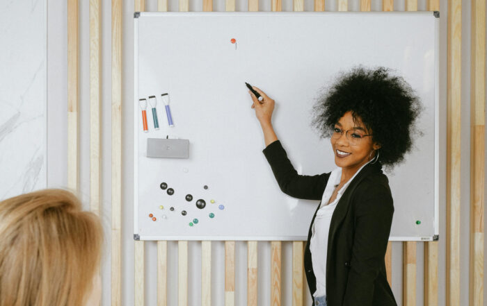 5 Ways to Influence People at Work image shows a smiling woman in business attire standing at a white board, marker raised to write something.