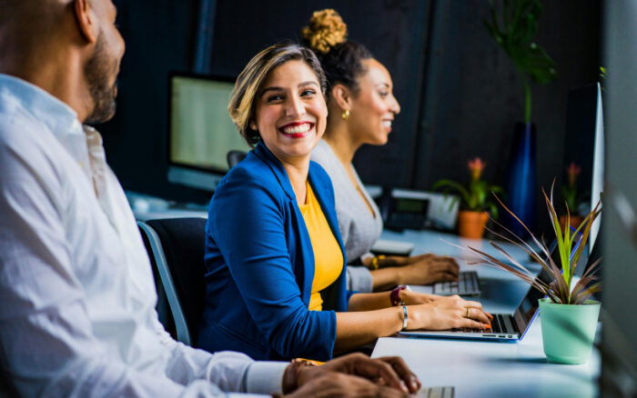 5 Ways to Boost Employee Engagment images shows a woman in a blue jacket sitting at a computer and grinning at the person next to her.