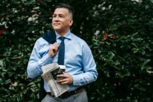 Refresh, Rejuvenate, and Restore Your Mind and Body This Spring image shows a man in a shirt and tie carrying his jacket over one shoulder and a newspaper and coffee in his other hand walking outside, looking peaceful.
