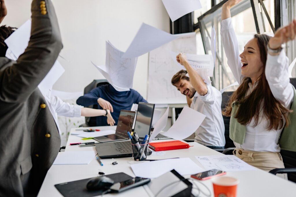 Tis the Season to Recognize a Job Well Done Image shows people in business attire sitting at a table with arms up celebrating.