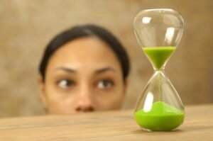 Woman looking at an hourglass which is at eye level on a table.