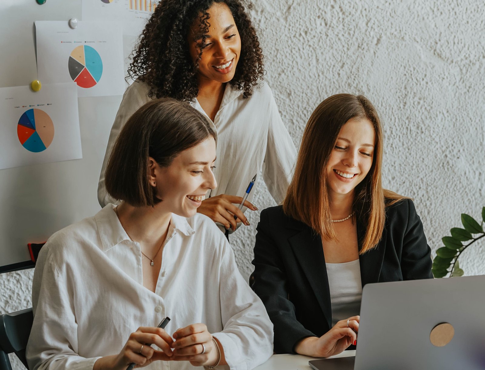 Three smiling women look at a computer screen.